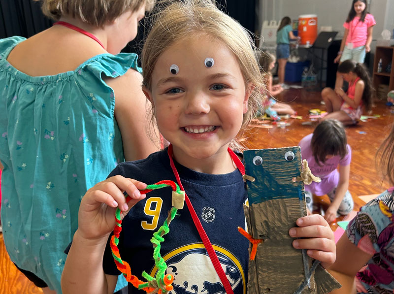 Smiling young girl with google eyes stickers on her forehead showing her crafts